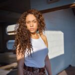 a woman with long curly hair standing in front of a white wall